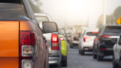 Close-up view from the rear of an orange pickup truck driving on a asphalt road. Cars were lined up in a long queue. With heavy traffic during rush hour in a Thailand city. The scene is daytime.