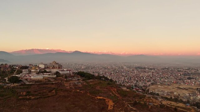 Aerial Drone Shot of Buddhist Monastery Above City with Mountain Range at Sunset