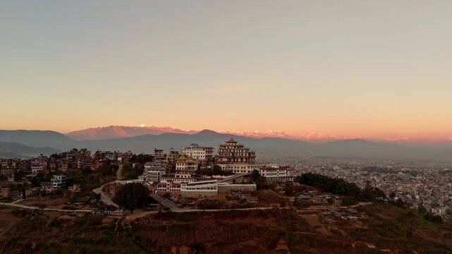 Aerial Drone Shot of Buddhist Monastery Above City with Mountain Range at Sunset