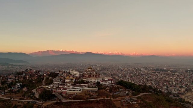 Aerial Drone Shot of Buddhist Monastery Above City with Mountain Range at Sunset