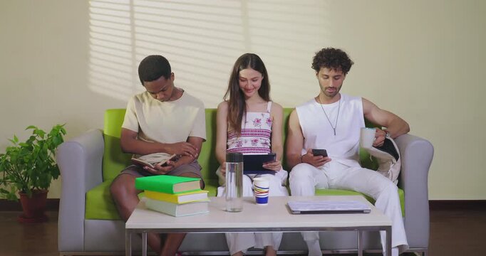 Indian young adult gen z male female girl sitting on couch sofa use tab look screen do new e learning study work indoor place happy teen man read book hold cup drink coffee talk enjoy day spend time