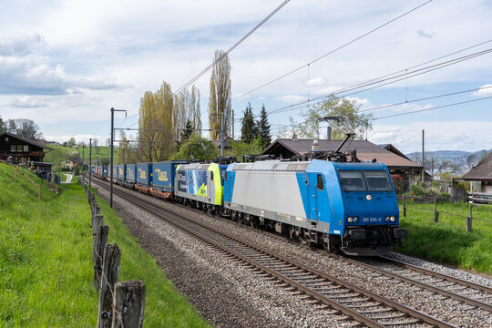 Spiez, Switzerland - April 27, 2023: Freight train in combined transport with LKW Walter trailers, hauled by double BLS locomotives near Spiez, set in the Swiss alpine landscape.