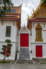 Vertical closeup of a traditional Thai temple building with white marble walls and striking red doors. A set of grey stone steps leads up to a central red door, which is framed by an ornate white arch