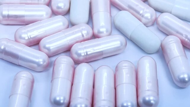 
4k slow moition video footage. Close-up view of shimmering pink and white medicinal capsules scattered on white surface.