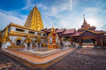 Fototapeta premium Stunning golden pagoda at Phutthakhaya Chedi in Sangkhla Buri, Kanchanaburi, Thailand shining beneath a dramatic blue sky
