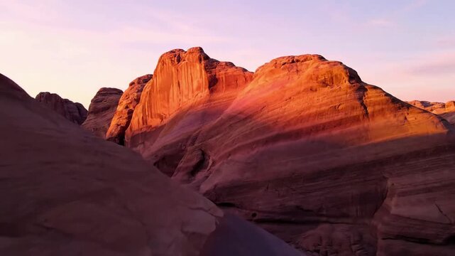 Soft Hues of Desert Geology Slow pan across a landscape of gentle, undulating rock formations, bathed in the initial golden and pink light of sunrise.
