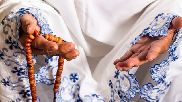a women wearing mukena is praying with prayer beads during fasting and eid mubarak