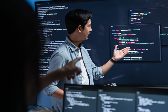 Asian Male software engineer pointing at source code on a large screen during a tech team meeting, explaining Code on the Screen, Discussing on coding task, New software development project in office.