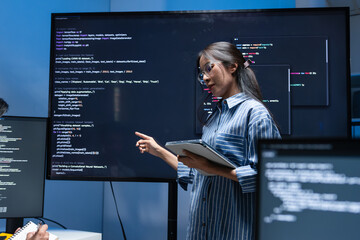 Asian Female Developer Presenting code on the screen, talking and discussing with team while...