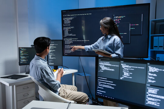 Asian Male software developer listening Female Developer Leader presenting code, Application development, feature update, AI Chatbot Project on monitor while software development meeting in office.