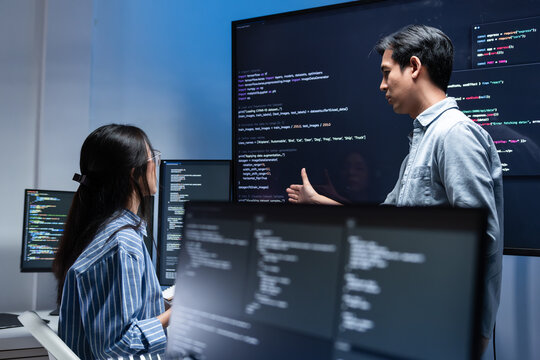 Software Developer Team working late in office at night. Programmer team collaboration, working on coding task, reviewing code while Male Programmer presenting code in the screen in tech office.