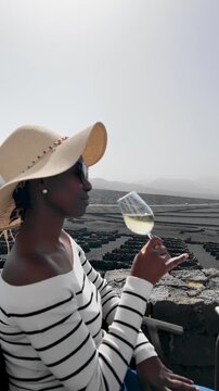 vertical tracking shot of a woman enjoying a glass of white wine amidst the unique volcanic vineyards of La Geria, Lanzarote 