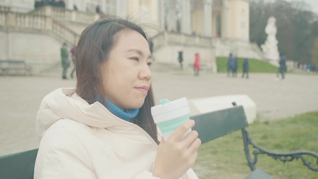 A person sits comfortably on a park bench, savoring a warm drink against a beautiful backdrop. The serene atmosphere and picturesque surroundings create a perfect moment for relaxation and enjoyment.