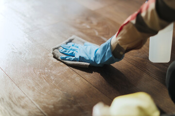 Person cleans wooden floor with cloth and spray bottle in home setting during day