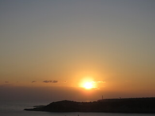 Beautiful Orange Sunrise breaking through clouds over the ocean and silhoutte of rocks with lighthouse