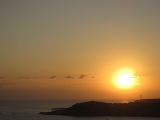 Fototapeta premium Beautiful Orange Sunrise breaking through clouds over the ocean and silhoutte of rocks with lighthouse