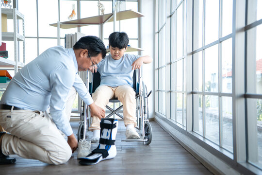 Father adjusting orthopedic ankle brace for young boy in wheelchair, highlighting family support and rehabilitation care