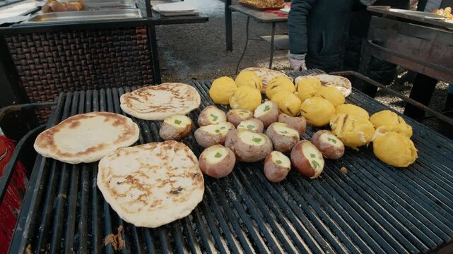 Stalls serve traditional food, Bread roll, potato with cheese and Bulz, polenta with cheese in a tourist train station. Steam rises from cooking as visitors enjoy fresh dishes at the marketplace.