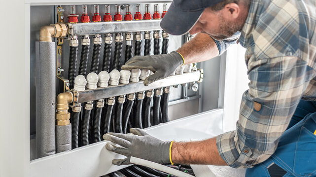The worker's hands adjusts and checks valves of a underfloor heating distributor. Underfloor heating.