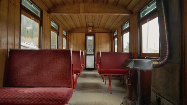 The inside of a Mocanita train carriage with red seats and a wood-burning stove. The vintage style captures the essence of old steam locomotives.