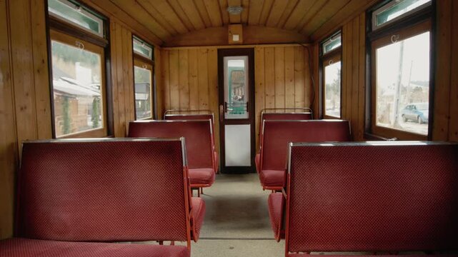 Inside a Mocanita train carriage with red seats and wooden walls. The view shows the interior as the train prepares for departure. Steam fills the air.