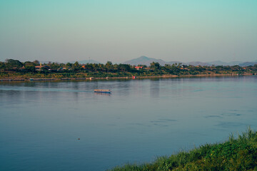 Fototapeta premium Longtail boat river mountain tree nature water transport travel landscape morning light Peaceful longtail boat wide river with soft morning light, green mountain background and riverside nature