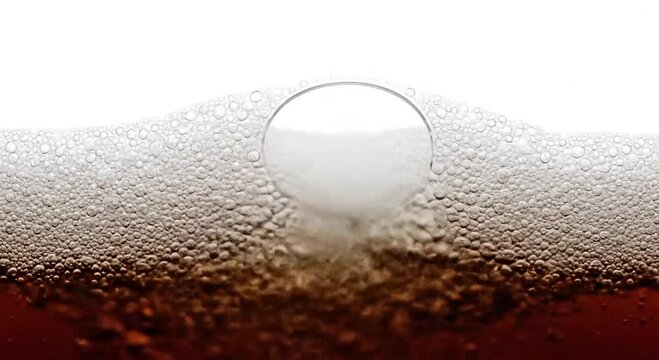 Close-up of numerous effervescent bubbles forming a frothy head on a brown carbonated drink