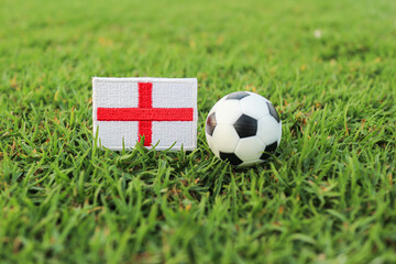 England national flag beside a soccer ball on green stadium grass with soft arena background, symbolizing global tournament heritage, football tradition, and national pride. © The Dell Shot by SJ