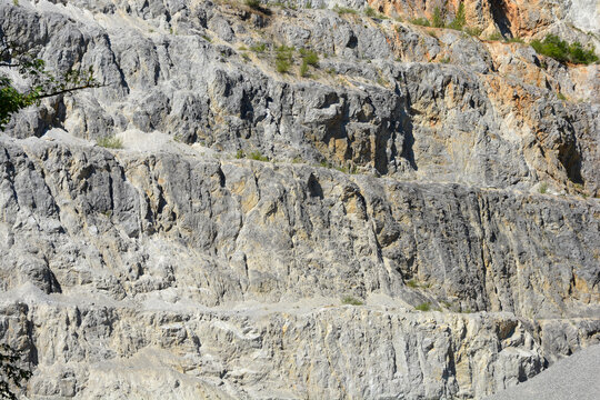 A close up shot of a massive stone quarry wall with detailed rocky layers and uneven textures under bright sunlight
