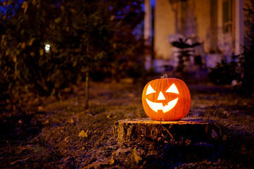 Traditional Jack-o-lantern glowing on a tree stump in a dark residential garden at dusk for Halloween decorations