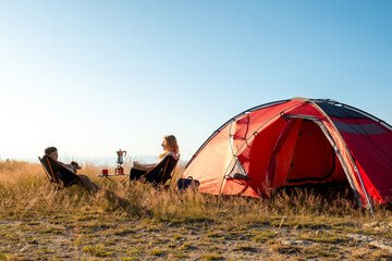 Morning evening ritual camping mountains mother son talking sitting chairs near red tent. Scenic wilderness background sun rays. Pet dog companion. Authentic travel experience family togetherness natu © marina_larina