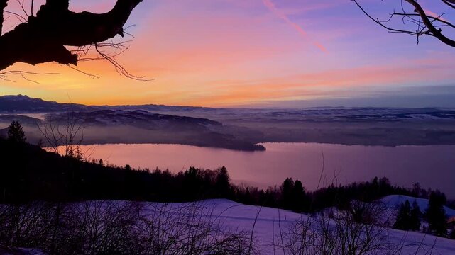 Intense winter sunset on Zugerberg overlooking Lake Zug, snow-covered landscape glowing under a dramatic red and golden evening sky.