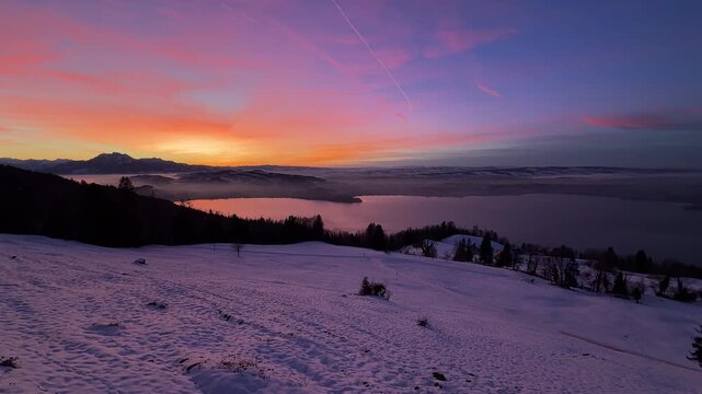 Intense winter sunset on Zugerberg overlooking Lake Zug, snow-covered landscape glowing under a dramatic red and golden evening sky.