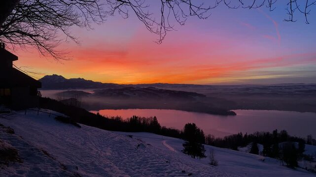 Intense winter sunset on Zugerberg overlooking Lake Zug, snow-covered landscape glowing under a dramatic red and golden evening sky.