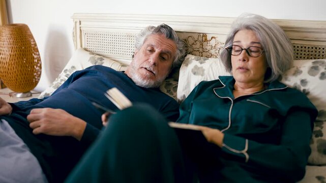 Mature husband and wife relaxing in the bedroom at night. Older people sharing a quiet moment, reading stories and talking before going to sleep
