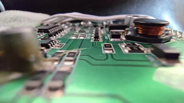 Macro panning shot of a green PCB circuit board, featuring detailed electronic components like capacitors, surface-mount resistors, and a copper inductor coil.
