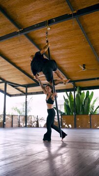 Athletic man and woman performing an acrobatic duet on a chinese pole. The couple showcases strength, flexibility, and teamwork in a studio. Vertical
