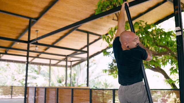 Bald athletic man practicing pole dancing in an outdoor gym. The focused artist is performing a graceful spinning routine on a vertical pylon