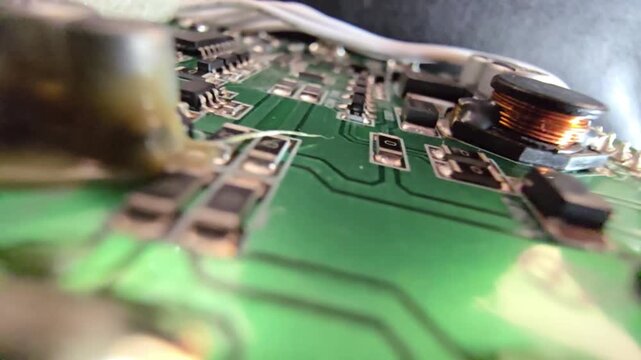 Macro panning shot of a green PCB circuit board, featuring detailed electronic components like capacitors, surface-mount resistors, and a copper inductor coil.