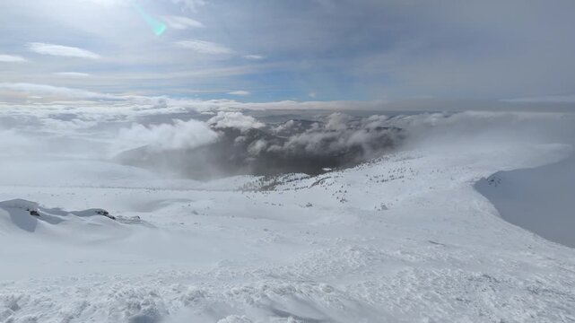 Snow-covered mountain landscape under cloudy sky with rolling clouds and distant forested slopes