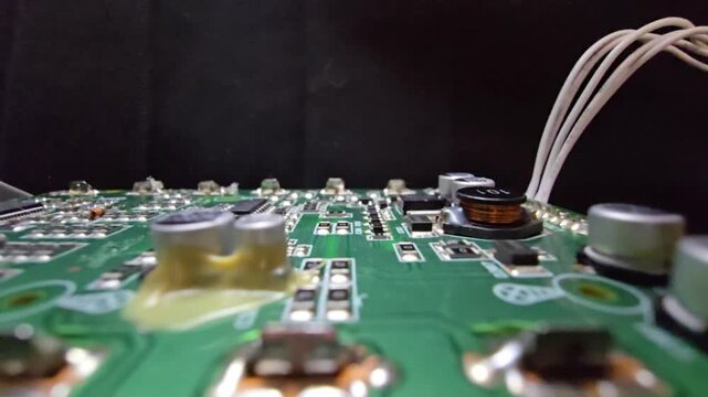 Macro of STM32 microchip on green PCB. Close-up of soldered white wires, electrolytic capacitors, inductors, and SMT components. High-tech circuit board for industrial hardware and engineering.