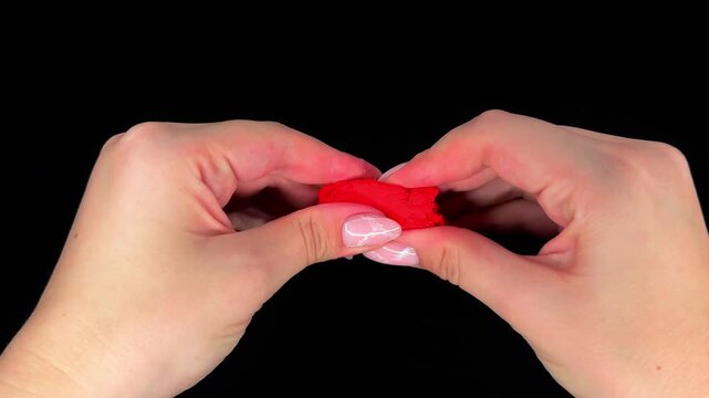 Hand kneads red modeling clay on a black background, developing ASMR video