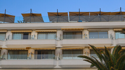 Modern resort building with glass balconies, retractable awnings and rooftop umbrellas, showcasing contemporary holiday architecture designed for relaxation, shade and comfortable outdoor living