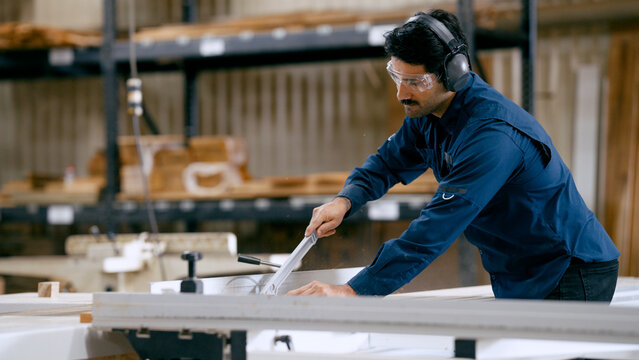 Skilled carpenter wearing safety gear, cutting wood planks in a busy workshop, focusing on craftsmanship and industry