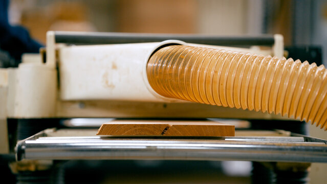 Woodworker processing timber using a thickness planer with a dust collection hose in a carpentry workshop, creating a smooth surface