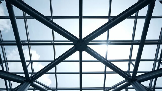 Modern glass roof structure with metal beams against blue sky