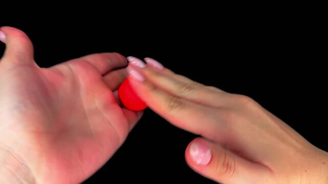 ASMR video: hand rolling red plasticine into a circle on a black background. Close-up, minimalism, texture and sensory effect for creativity and relaxation.