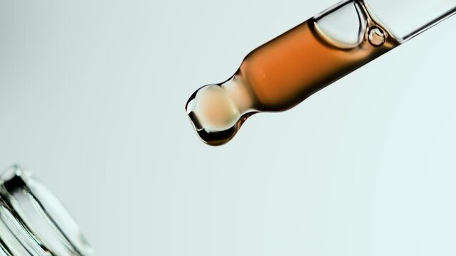 Macro close-up of a transparent glass dropper filled with amber serum rising from a cosmetic bottle. A single droplet falls before the pipette returns inside, emphasizing texture and precision.