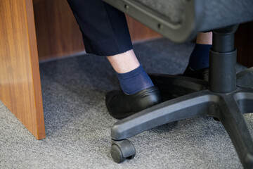 Low section view of male feet in black shoes and trousers under an office table. Clerk or manager...