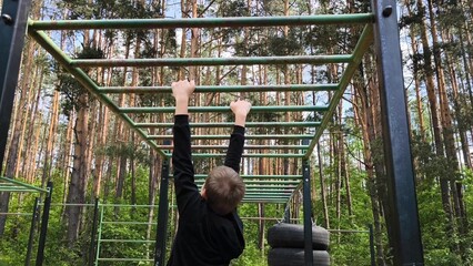 Obraz premium Young guy, Teenager, is playing sports on a horizontal bar on an outdoor playground. Boosts strength and endurance. sports on the horizontal bar. Rear view
